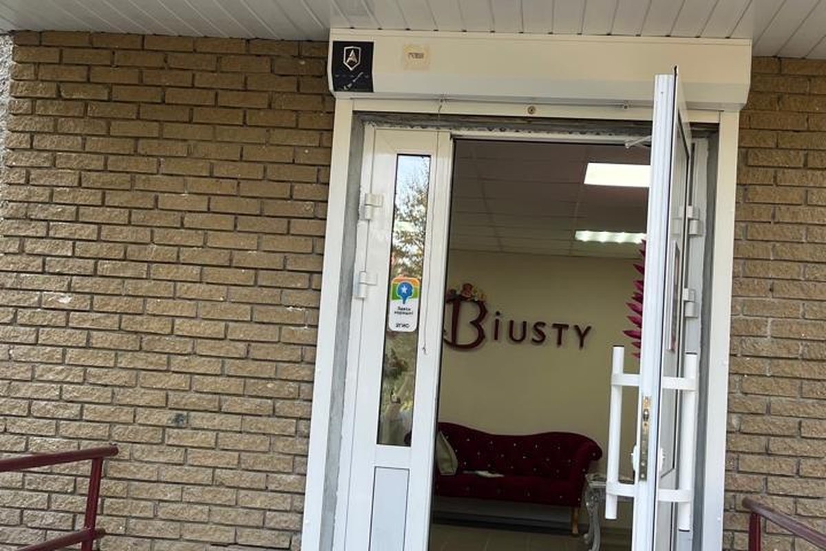 Открытая дверь салона в кирпичном доме, внутри видна вывеска Biusty и освещённый зал